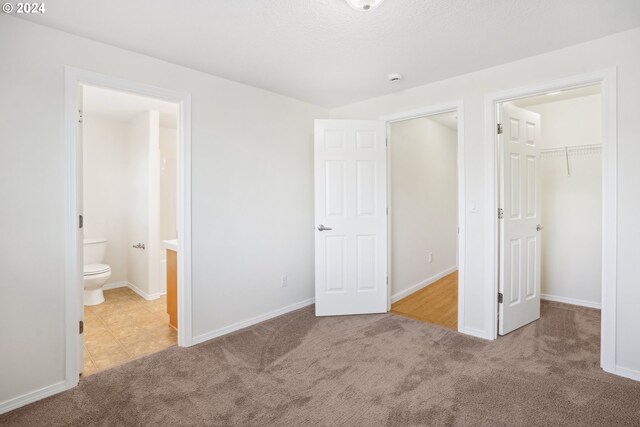 unfurnished bedroom featuring a closet, a walk in closet, light carpet, and ensuite bathroom