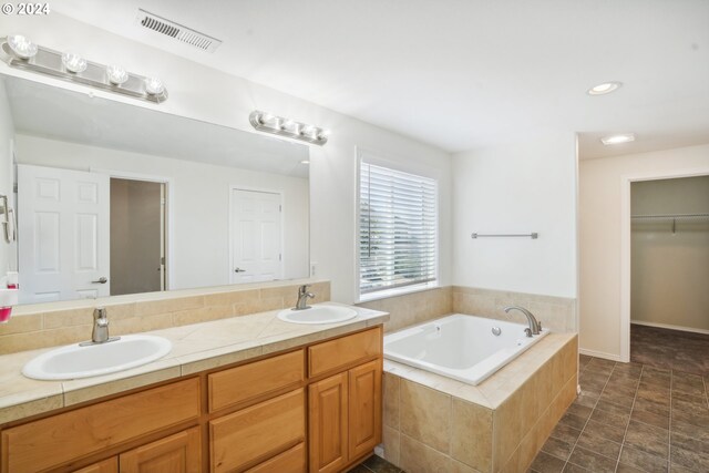 bathroom with tile patterned flooring, tiled tub, and vanity