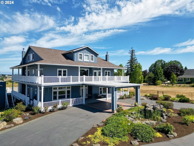 rear view of property with driveway, a balcony, a porch, and a chimney