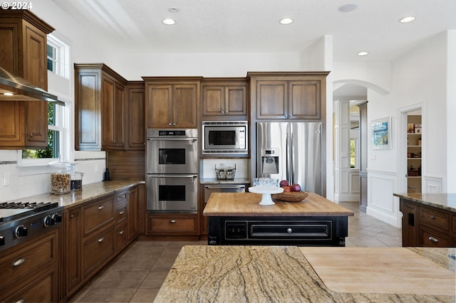 kitchen featuring tile patterned floors, stainless steel appliances, arched walkways, and tasteful backsplash