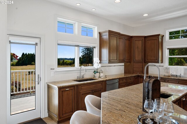 kitchen with plenty of natural light, stainless steel dishwasher, sink, and light stone countertops