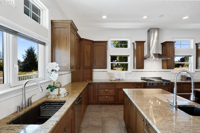 kitchen with backsplash, sink, light stone countertops, and wall chimney range hood