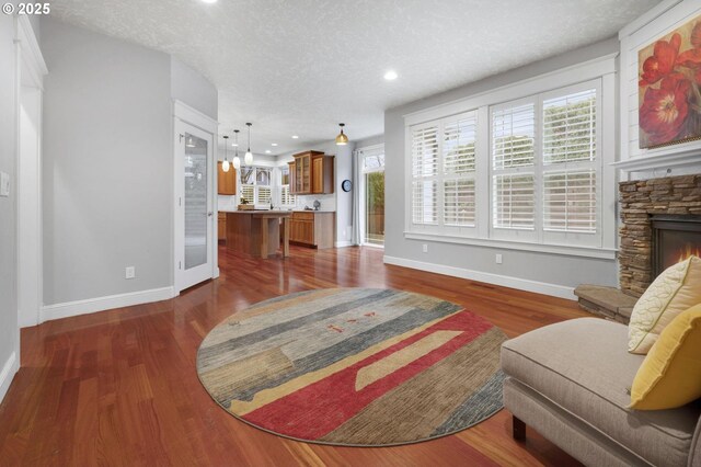 living room featuring a textured ceiling, a stone fireplace, and dark wood-type flooring