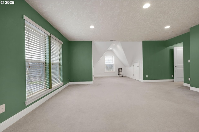 additional living space with a textured ceiling, light colored carpet, and lofted ceiling