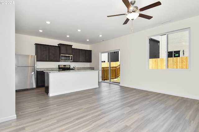 kitchen with dark brown cabinets, light hardwood / wood-style flooring, an island with sink, and appliances with stainless steel finishes