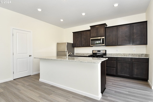 kitchen featuring stainless steel appliances, a kitchen island with sink, dark brown cabinetry, and light wood-type flooring