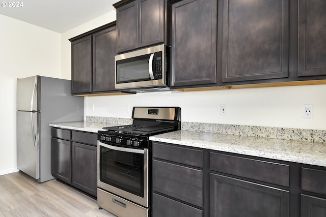 kitchen with dark brown cabinetry, appliances with stainless steel finishes, light stone countertops, and light hardwood / wood-style flooring