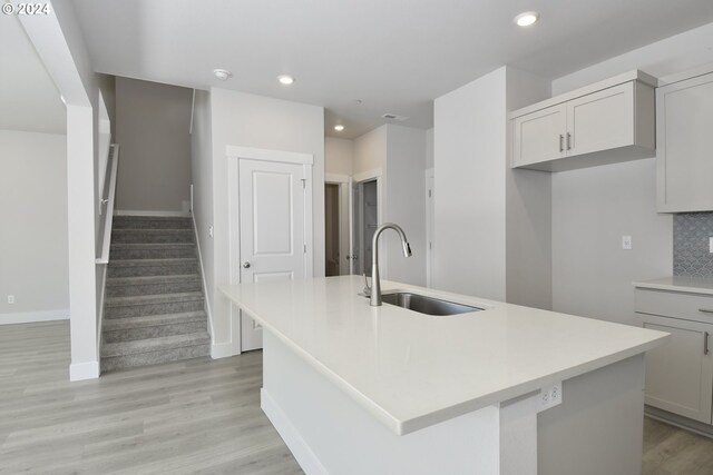 kitchen with sink, an island with sink, backsplash, and light hardwood / wood-style floors