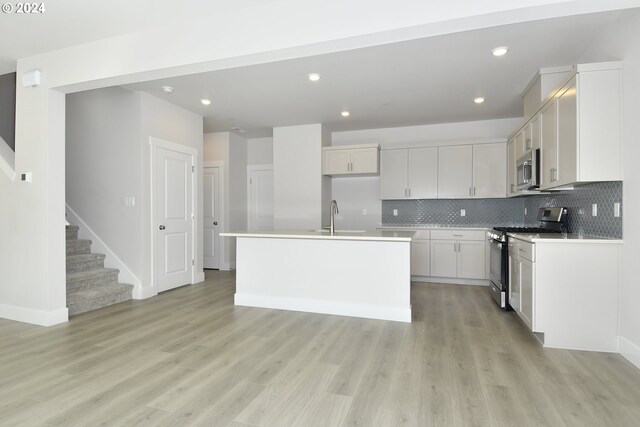 kitchen featuring backsplash, white cabinetry, light hardwood / wood-style floors, stainless steel appliances, and a center island with sink