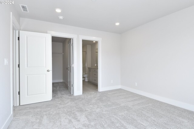 unfurnished bedroom with light carpet, a walk in closet, a closet, and ensuite bath