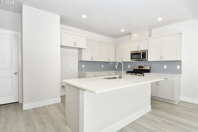 kitchen featuring light hardwood / wood-style flooring, stainless steel appliances, backsplash, a center island with sink, and sink