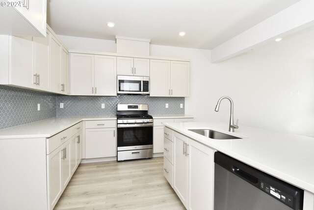 kitchen featuring decorative backsplash, white cabinets, appliances with stainless steel finishes, light hardwood / wood-style floors, and sink