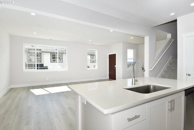 kitchen featuring sink, light hardwood / wood-style floors, stainless steel dishwasher, white cabinets, and a center island with sink