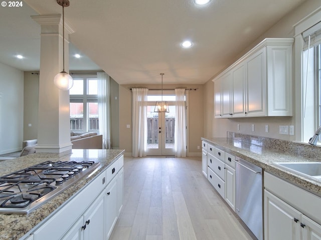 kitchen with decorative light fixtures, stainless steel appliances, white cabinetry, and light hardwood / wood-style flooring