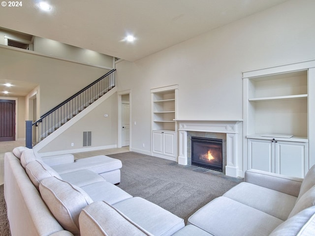 carpeted living room featuring built in shelves, a fireplace, and a towering ceiling