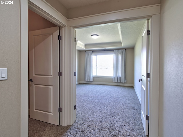 hall featuring carpet flooring, a tray ceiling, and a textured ceiling