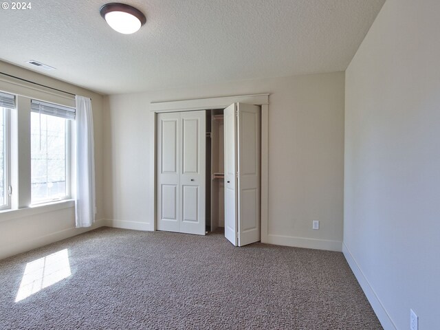 unfurnished bedroom with carpet flooring, a textured ceiling, and a closet