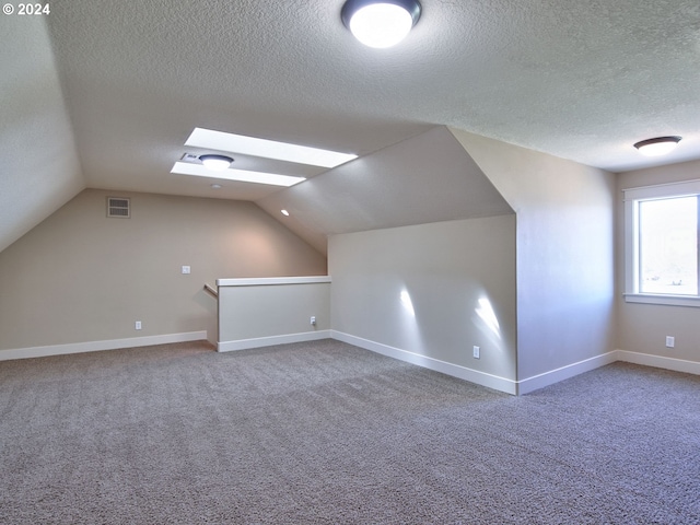 additional living space featuring carpet, lofted ceiling with skylight, and a textured ceiling