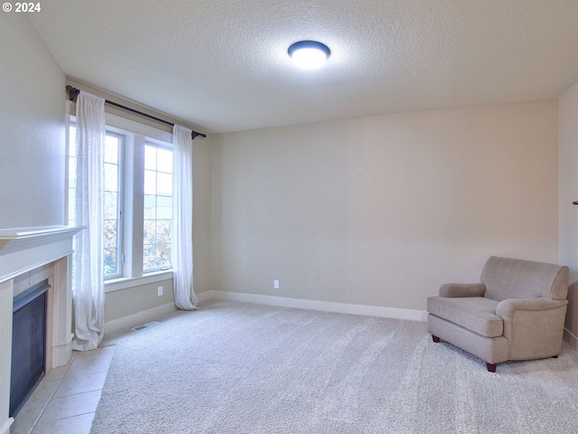 unfurnished room featuring a tiled fireplace, light colored carpet, and a textured ceiling