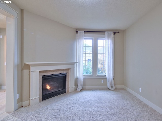 unfurnished living room featuring a textured ceiling, light colored carpet, and a tiled fireplace