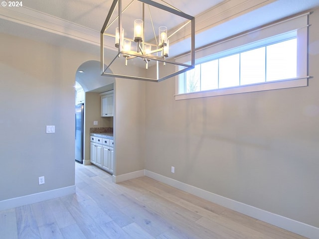 unfurnished dining area featuring an inviting chandelier, ornamental molding, and light hardwood / wood-style flooring