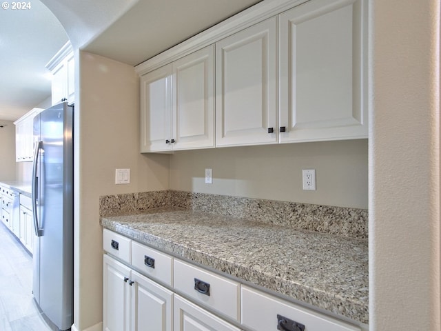 kitchen featuring stainless steel refrigerator, light stone counters, light hardwood / wood-style flooring, and white cabinets