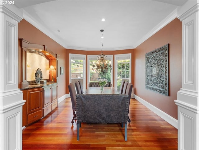 dining room featuring ornamental molding, decorative columns, a notable chandelier, and wood-type flooring