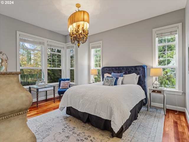 bedroom with multiple windows, an inviting chandelier, and hardwood / wood-style flooring