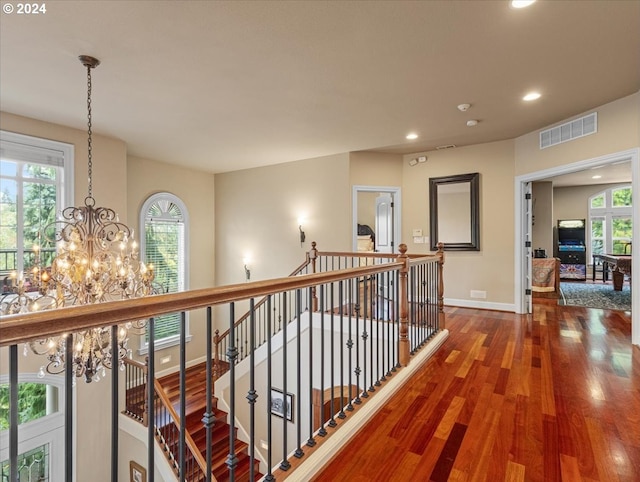 corridor with a wealth of natural light, a notable chandelier, and hardwood / wood-style flooring