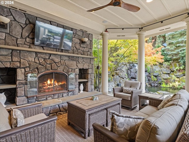 sunroom featuring an outdoor stone fireplace, ceiling fan, and decorative columns