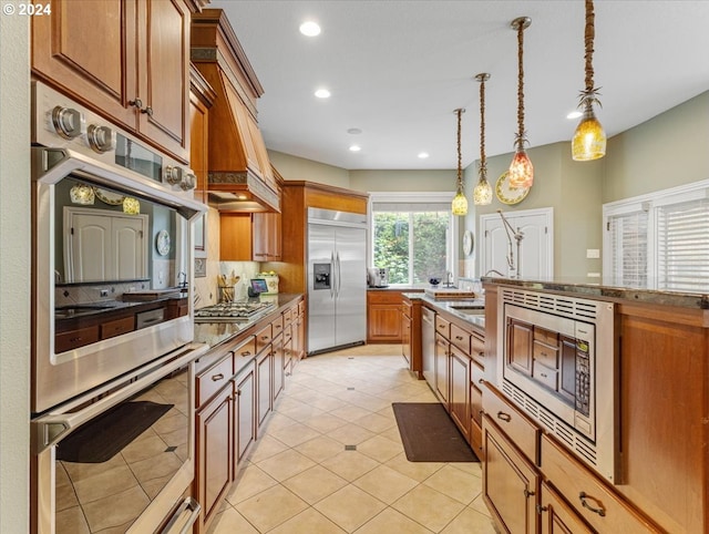 kitchen featuring tasteful backsplash, light tile patterned flooring, hanging light fixtures, built in appliances, and premium range hood