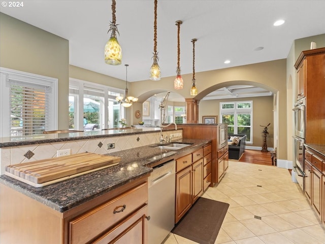 kitchen featuring appliances with stainless steel finishes, a spacious island, dark stone countertops, sink, and decorative light fixtures