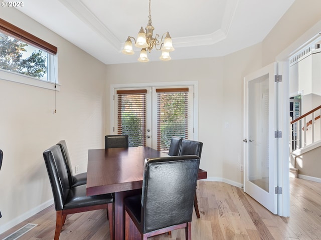 dining room with a chandelier, french doors, a tray ceiling, and light hardwood / wood-style flooring