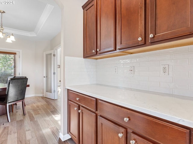 kitchen featuring light wood-type flooring, light stone counters, a raised ceiling, decorative light fixtures, and a chandelier