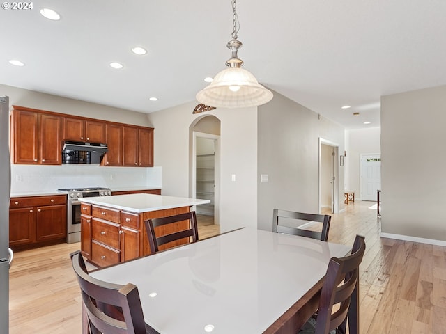 kitchen with high end stainless steel range, a center island, decorative light fixtures, and light hardwood / wood-style flooring