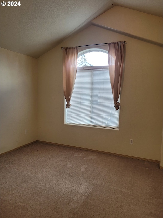 empty room featuring a textured ceiling, vaulted ceiling, and carpet floors