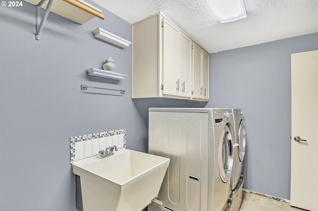 laundry area with a textured ceiling, cabinets, sink, and washing machine and clothes dryer