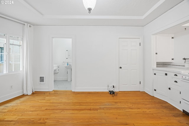 unfurnished dining area featuring a tray ceiling, heating unit, light wood-style flooring, and baseboards