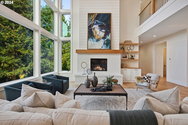 living room featuring a large fireplace, plenty of natural light, a towering ceiling, and light wood-type flooring