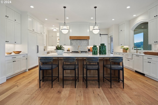 kitchen with premium range hood, a kitchen island with sink, a kitchen breakfast bar, white cabinets, and decorative light fixtures