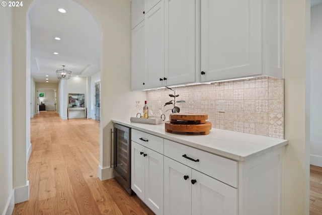 bar featuring tasteful backsplash, light stone counters, light hardwood / wood-style floors, white cabinets, and beverage cooler