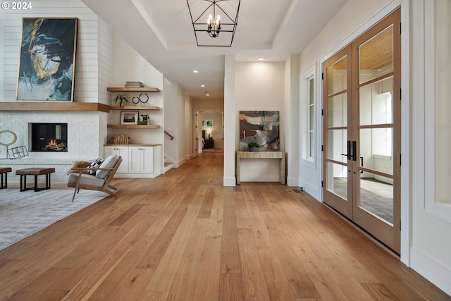 hallway featuring french doors, a chandelier, light wood-type flooring, and a tray ceiling