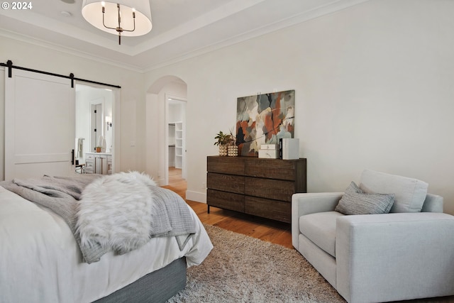 bedroom with a raised ceiling, crown molding, a barn door, and light hardwood / wood-style flooring