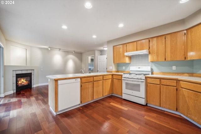 kitchen featuring a tiled fireplace, sink, kitchen peninsula, white appliances, and dark hardwood / wood-style flooring