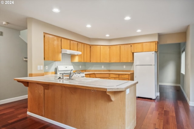 kitchen featuring sink, a breakfast bar, kitchen peninsula, white appliances, and dark wood-type flooring