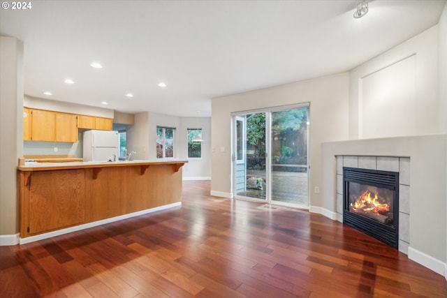 kitchen with a kitchen bar, dark hardwood / wood-style flooring, a tiled fireplace, white refrigerator, and light brown cabinetry