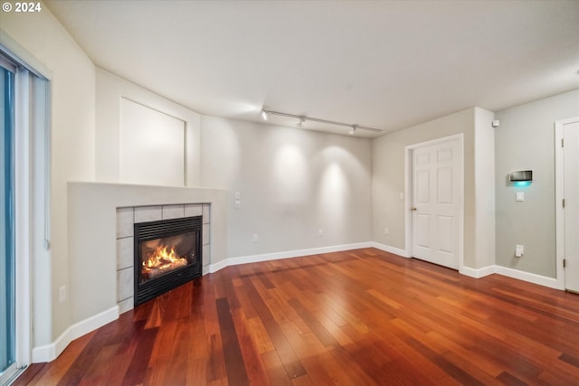 unfurnished living room with a tiled fireplace, wood-type flooring, and track lighting