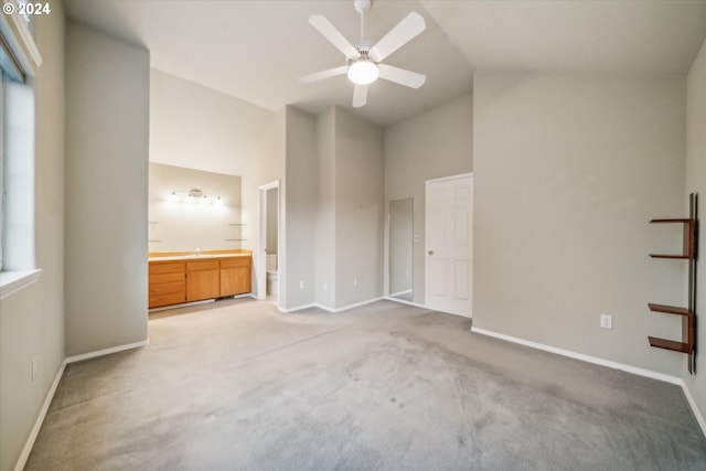 unfurnished bedroom featuring high vaulted ceiling, light carpet, ceiling fan, and ensuite bathroom