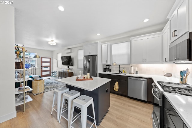 kitchen with sink, stainless steel appliances, a center island, white cabinets, and a kitchen bar