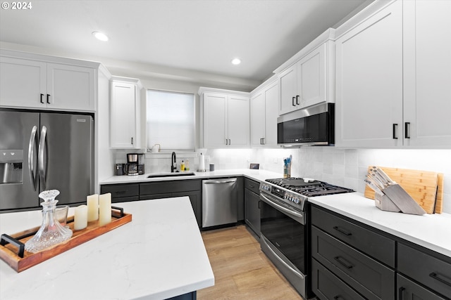 kitchen featuring appliances with stainless steel finishes, white cabinets, light wood-type flooring, sink, and tasteful backsplash